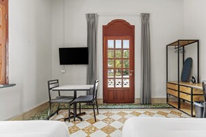 Una habitación con puerta de madera, televisor montado en la pared, una mesa con sillas y una cama con colcha estampada.