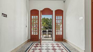 A hallway with a checkered floor, a view of a balcony with a table and chairs, and a door with a number sign.