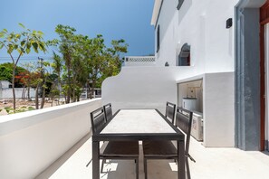 Un patio al aire libre con una mesa y sillas, una pared blanca y una vista de árboles y un edificio al fondo.