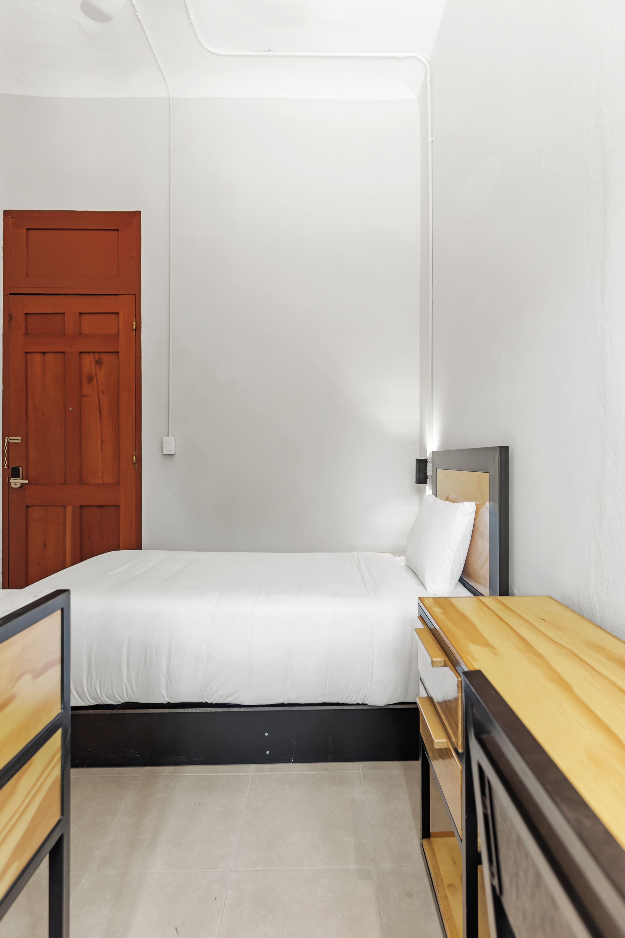 Une chambre à coucher minimaliste avec un lit simple, une table de chevet en bois, un bureau et une porte.