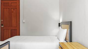 Une chambre à coucher minimaliste avec un lit simple, une table de chevet en bois, un bureau et une porte.