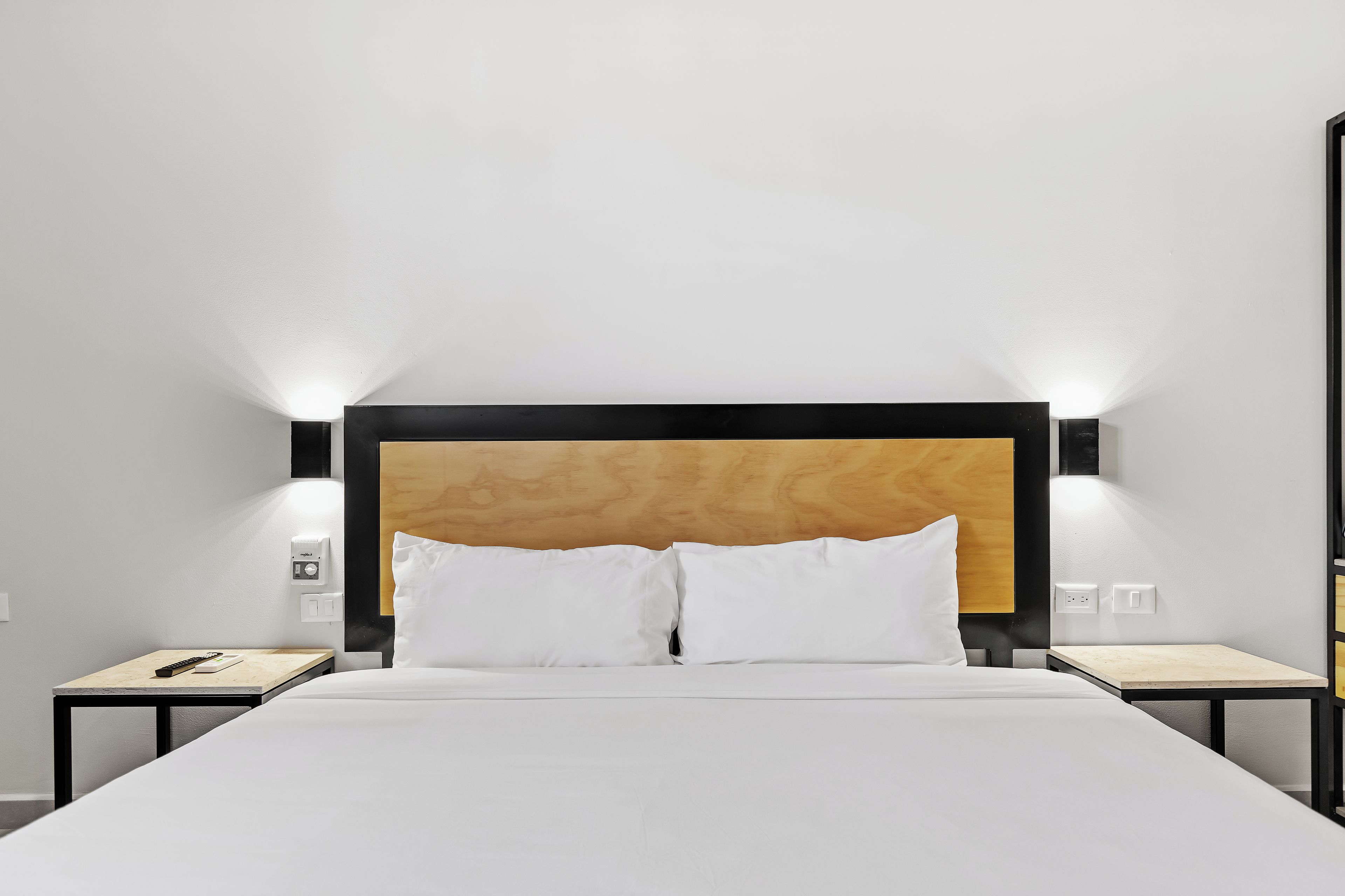 Een hotelkamer met een groot bed, twee nachtkastjes, een houten hoofdeinde en wandlampen.
