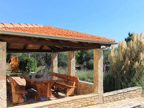 A covered outdoor seating area with a stone table and benches, surrounded by stone walls and vegetation. - Holiday Home in Pavicini With Swimming Pool (Marcana)