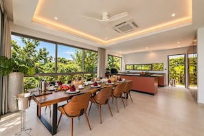 A modern kitchen with a dining area, large windows, and a view of greenery. - Sol Sofia 4BR/Seaview/Pool/BF/Staffs (Koh Samui)