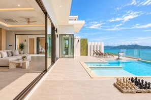 A modern hotel room with a large window, a pool, and a chess set. - Sol Sofia 4BR/Seaview/Pool/BF/Staffs (Koh Samui)