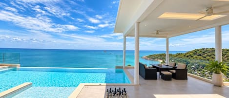A pool with a chessboard, outdoor seating, and a view of the sea.