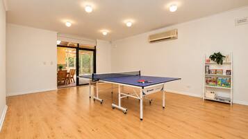 Une pièce avec une table de ping-pong, un plancher en bois, une bibliothèque remplie de livres et d’objets décoratifs, et une porte donnant sur un espace extérieur.