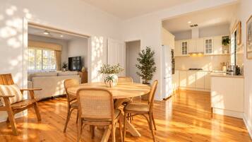 Une cuisine moderne avec des meubles blancs, un coin repas avec une table et des chaises en bois, et un salon avec un canapé et un téléviseur.