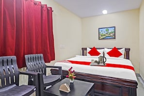 Ein Hotelzimmer mit einem Bett, zwei Stühlen, einem kleinen Tisch, einer Vase mit Blumen und einem Gemälde an der Wand.