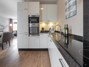 A modern kitchen with built-in appliances, a dining area with a table and chairs, and a bar area with bottles. - Luxury villa with private wellness (Colijnsplaat)