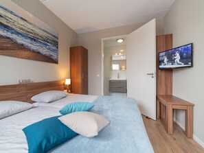 A hotel room with a bed, a television, a painting, and a bathroom visible through an open door. - Luxury villa with private wellness (Colijnsplaat)