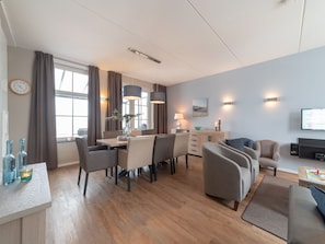 A modern living room with a dining area, wooden flooring, and a flat-screen TV mounted on the wall. - Luxury villa with private wellness (Colijnsplaat)