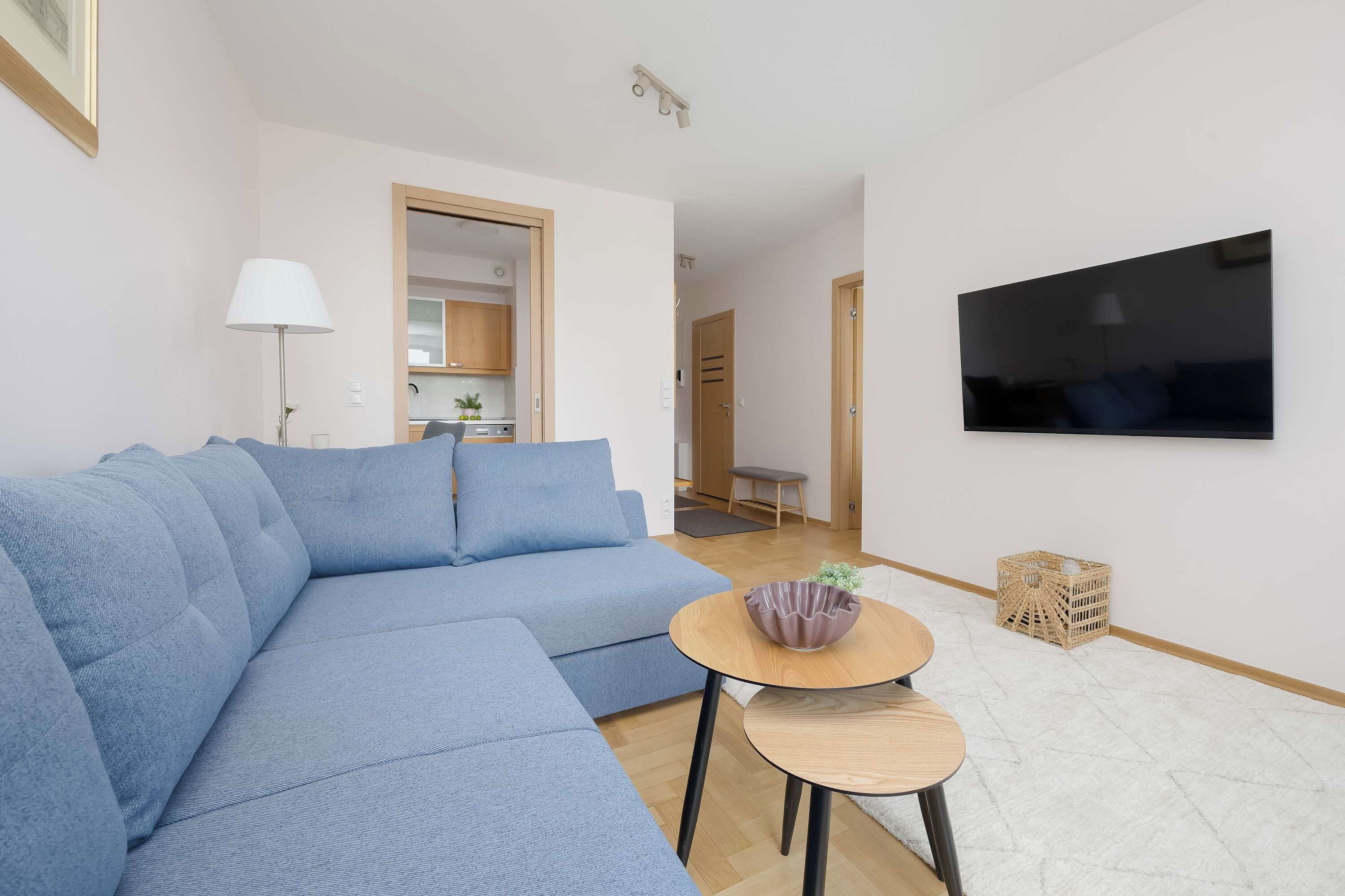 Una sala de estar moderna con un sofá seccional, un televisor de pantalla plana montado en la pared, una mesita redonda con un cuenco y una cesta de mimbre.
