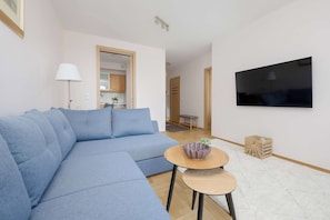 Una sala de estar moderna con un sofá seccional, un televisor de pantalla plana montado en la pared, una mesita redonda con un cuenco y una cesta de mimbre.