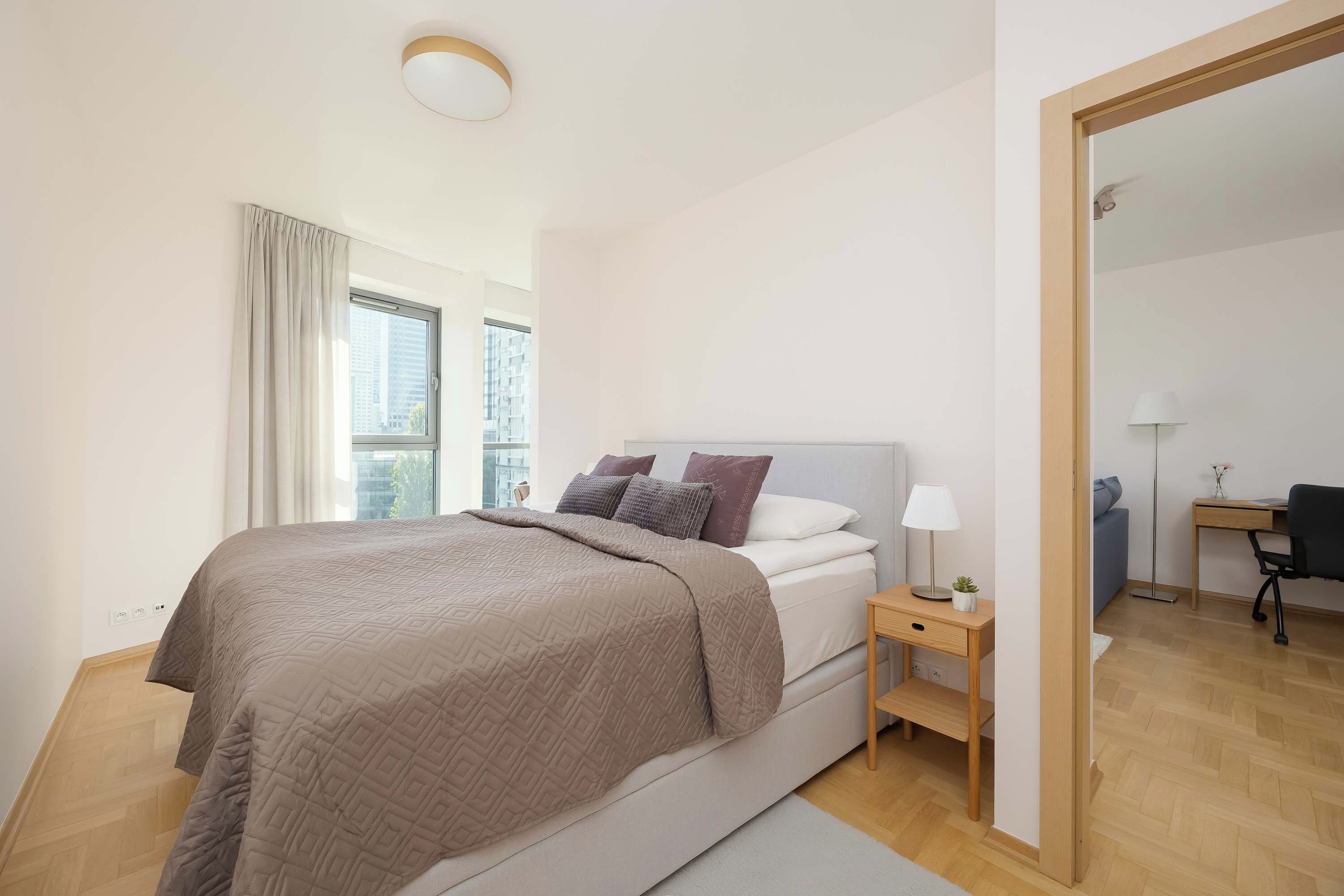 A modern bedroom with a large bed, bedside tables, a desk, and a mirror.
