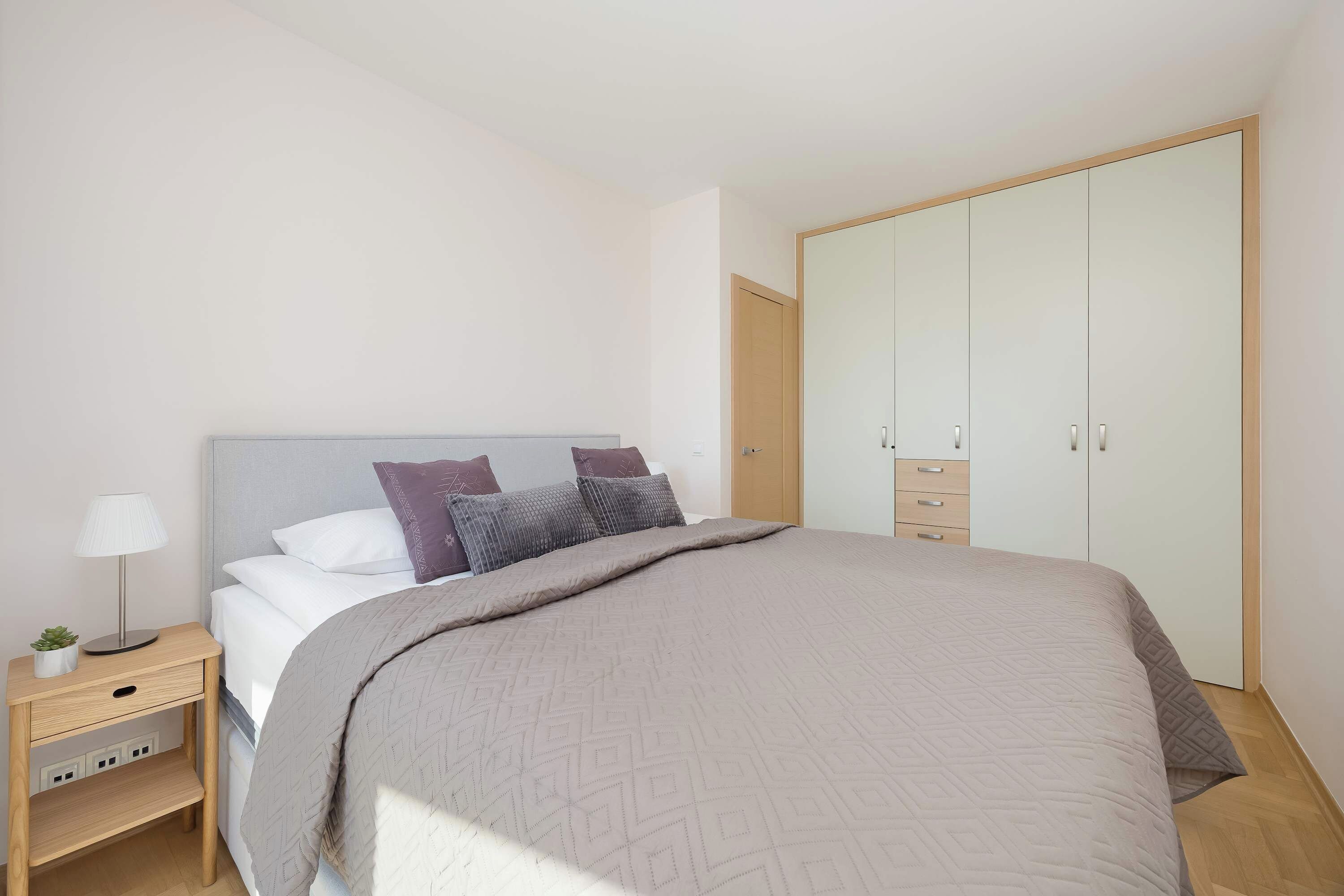 Un dormitorio con cama, mesita de noche, lámpara y armario.