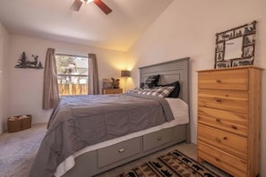 Een slaapkamer met een bed, een dressoir, een nachtkastje, een lamp en een raam met gordijnen.