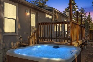 A hot tub in front of a house with a wooden deck and a light fixture on the wall. - Private Hot Tub + Fireplace, 5 Min to Slopes, Fenced Yard, Sleeps 8 (Big Bear)