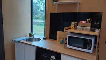 Eine kompakte Küche mit Spüle, Mikrowelle, Tee-Ecke und einem Fenster mit Blick auf Grünflächen.