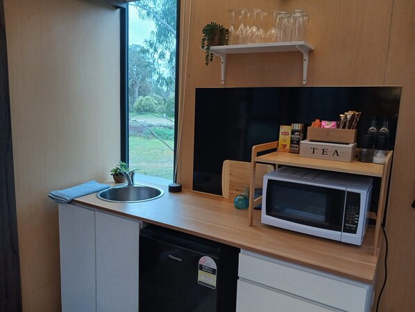 A compact kitchen with a sink, a microwave, a tea station, and a window with a view of greenery.