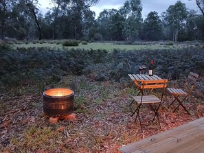 An outdoor seating area with a table and chairs, a portable heater, and a bottle of wine.