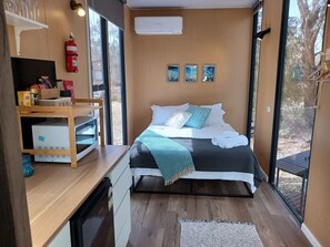 A modern bedroom with a bed, bedside table, and a view of the outdoors.