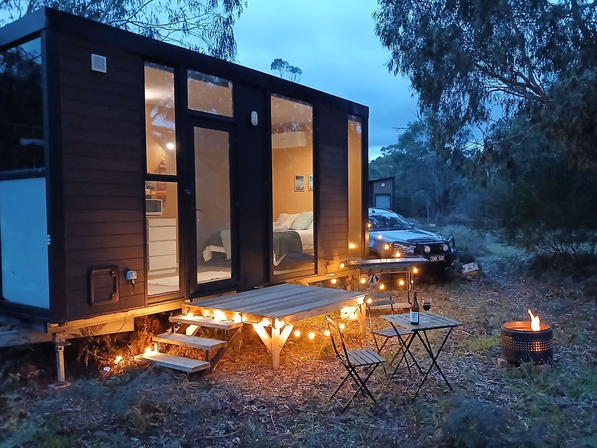 A modern cabin with a deck, outdoor seating, and a fire pit.