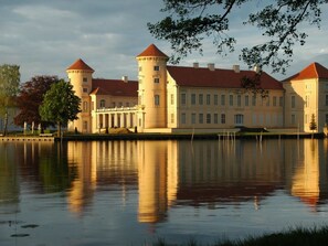 A large, historic building with multiple towers and a reflective water body in front. - Forester's House at Linowsee (Rheinsberg)