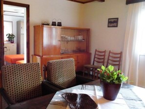 A dining area with patterned chairs, a table with a white tablecloth, a potted plant, and a wooden cabinet with glassware. - Forester's House at Linowsee (Rheinsberg)