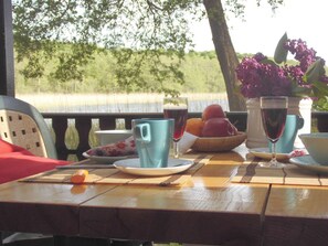 A table set outdoors with a view of a natural landscape, featuring a bowl of fruit, a glass of red wine, and a blue mug. - Forester's House at Linowsee (Rheinsberg)