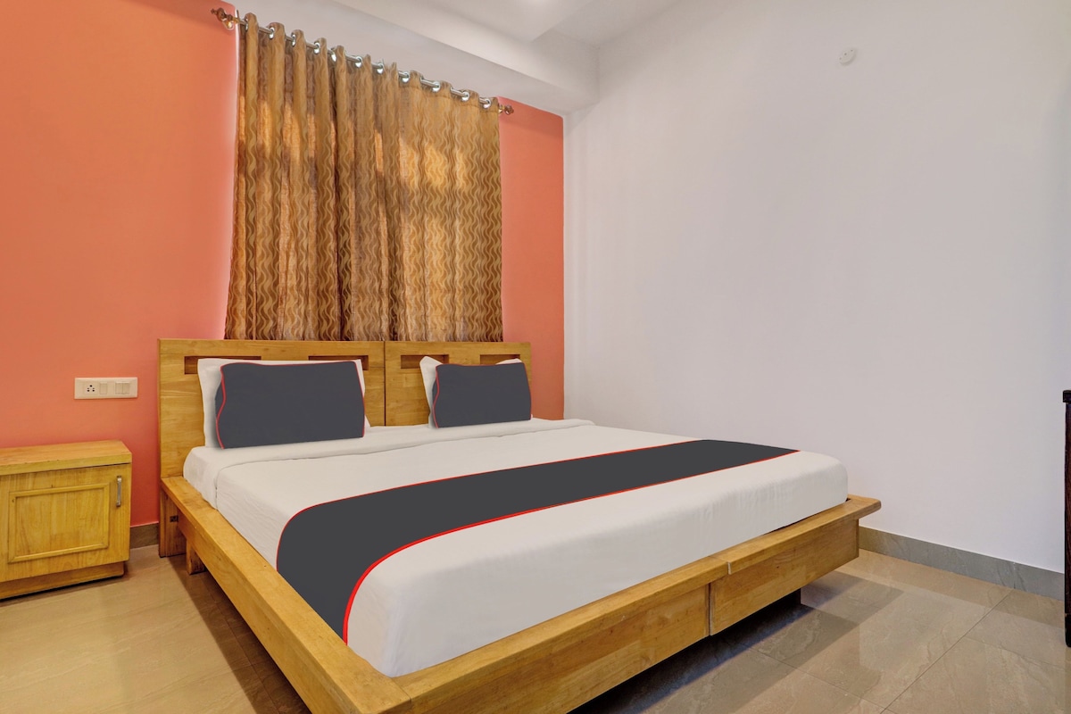 A bedroom with a wooden bed, a nightstand, a wall-mounted light, and a curtain.