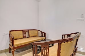 A corner room with a wooden sofa and a wooden chair. - Capital O Qualia Gachibowli (Hyderabad)