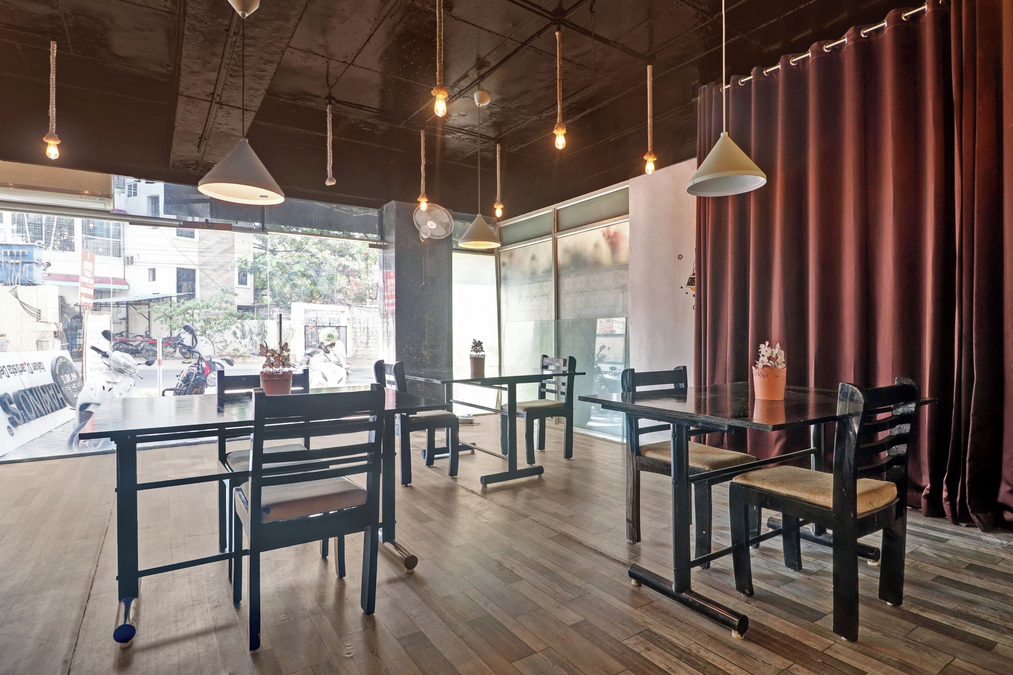 A restaurant interior with wooden tables and chairs, hanging pendant lights, and a view of the street outside.