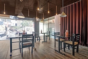A restaurant interior with wooden tables and chairs, hanging pendant lights, and a view of the street outside. - Capital O Qualia Gachibowli (Hyderabad)