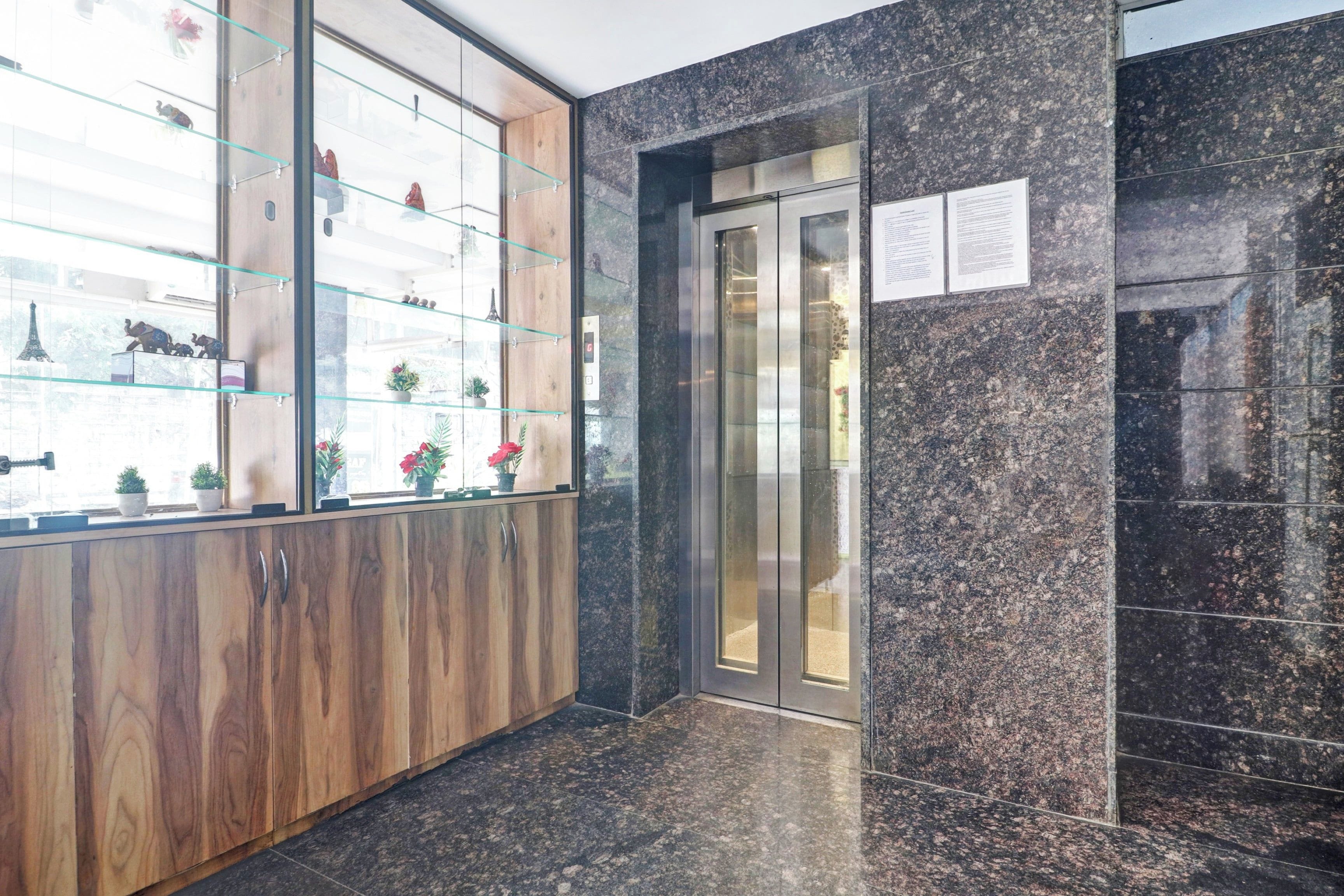 Een receptiegedeelte met een houten kast, een glazen vitrine met decoratieve objecten en een marmeren muur.