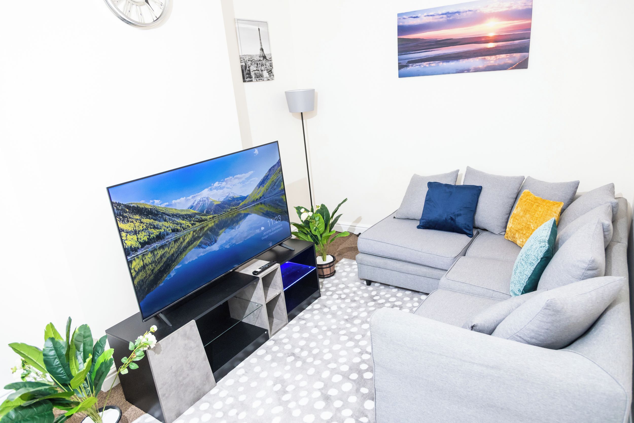 A modern living room with a flat-screen TV, grey sofa, and a polka dot rug.