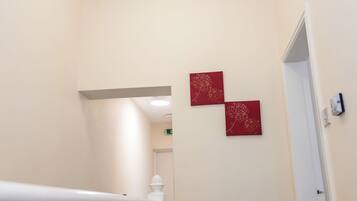 A hallway with a white railing, a door at the end, and two red wall decorations.