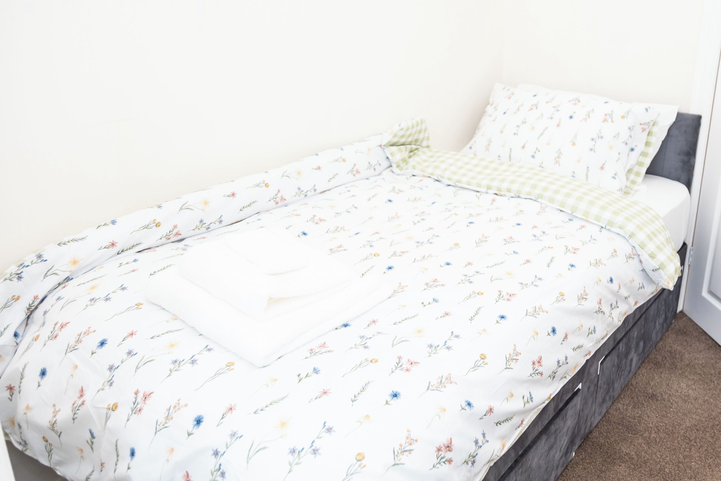 A bed with a floral-patterned bedspread and pillows, a checkered blanket, and a dark headboard.