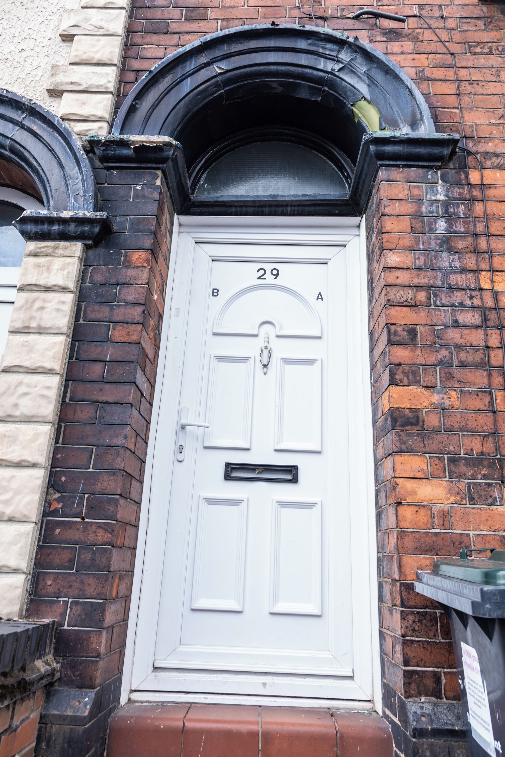 A white door with the number 29, flanked by brick walls and a black archway.