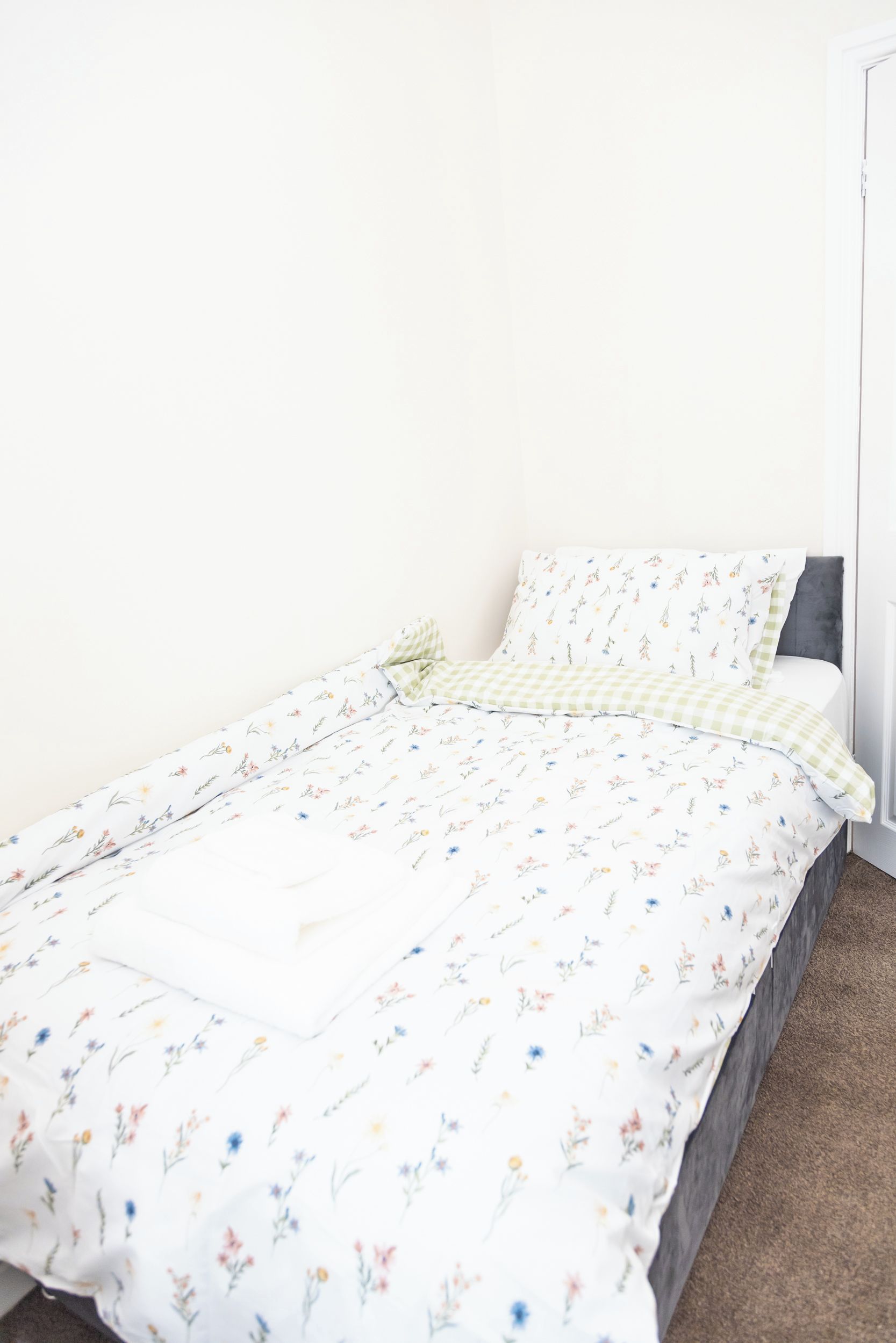 A single bed with a floral-patterned bedspread and a checkered pillow.