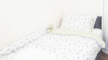 A single bed with a floral-patterned bedspread and a checkered pillow.
