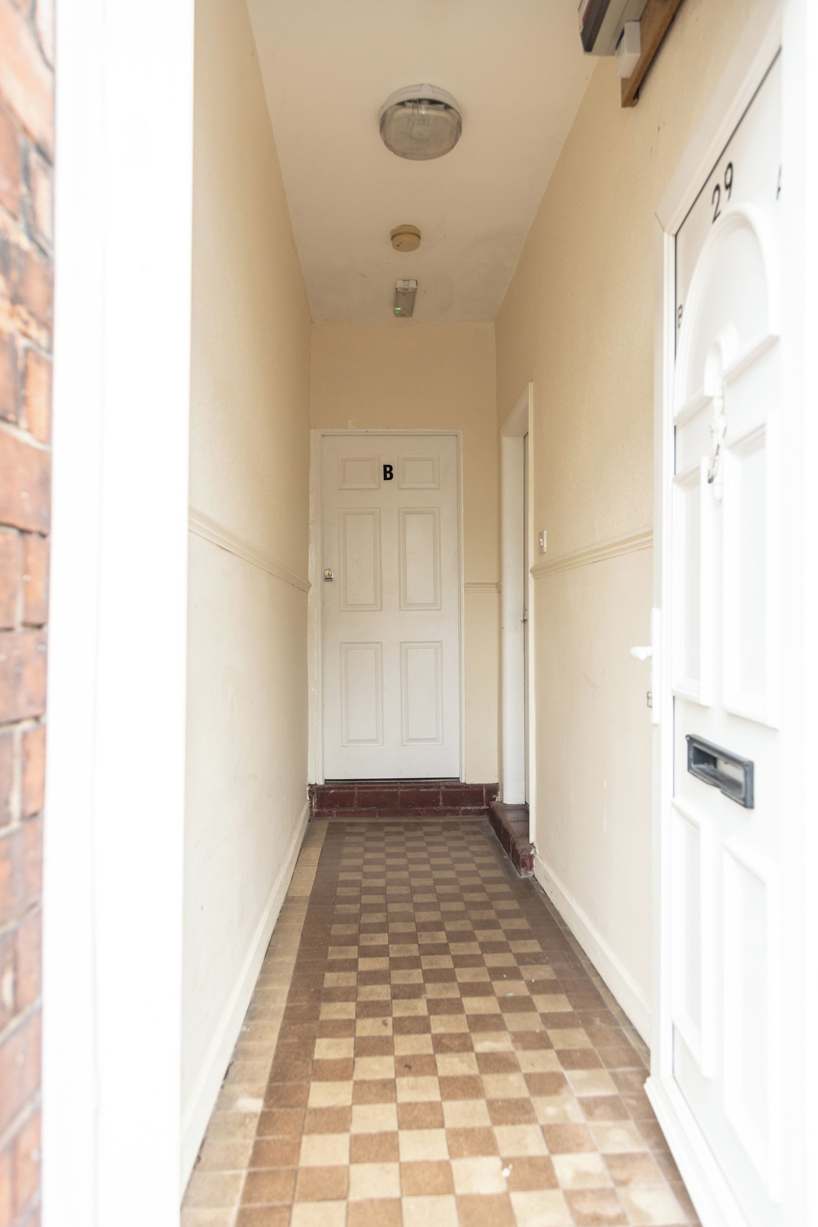 A hallway with a checkered floor, a white door with a number, and a mailbox.