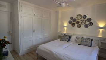 Un dormitorio con cama, armario blanco, ventilador de techo, luces fijadas en la pared y placas decorativas.