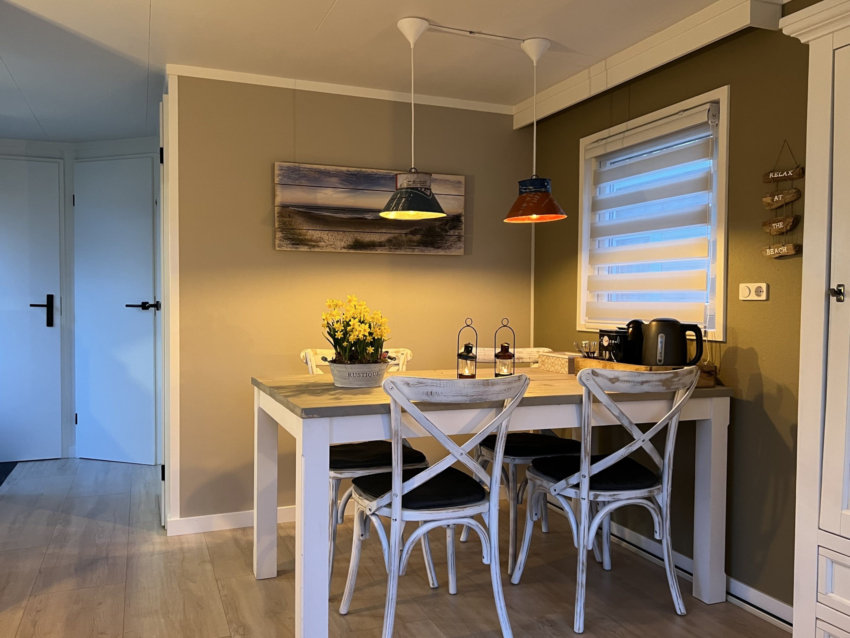 A dining area with a table, chairs, a potted plant, and a painting on the wall.