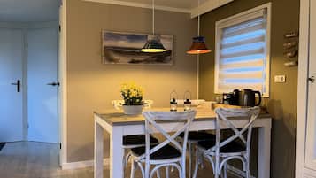 A dining area with a table, chairs, a potted plant, and a painting on the wall.