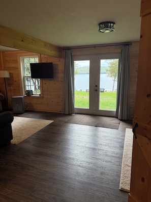 Une pièce au décor intérieur en bois, un téléviseur fixé au mur, une grande fenêtre donnant sur un lac et une porte-fenêtre coulissante.