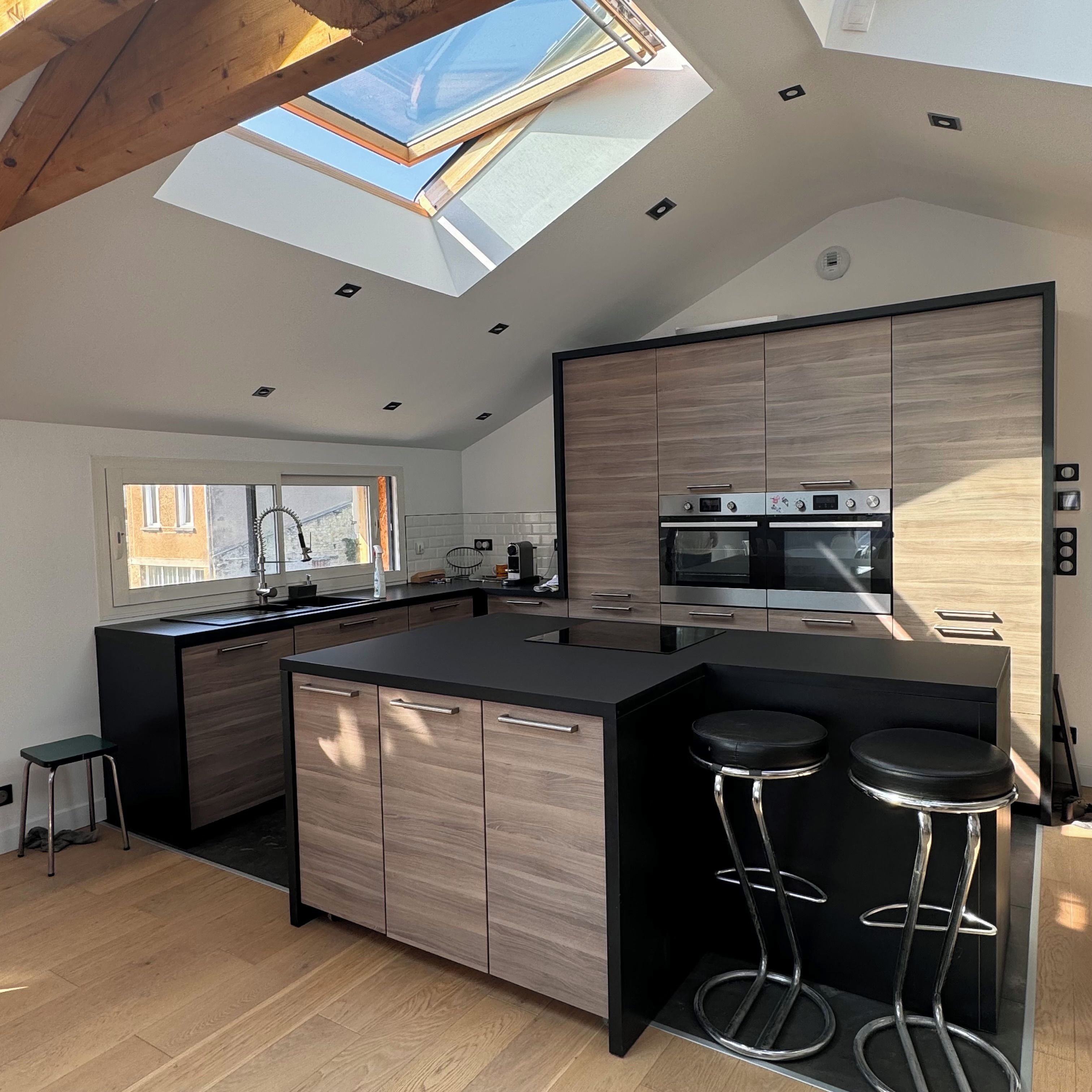 A modern kitchen with a skylight, wooden cabinets, and a central island with stools.