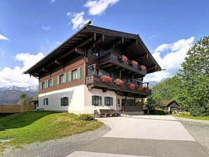 En toetagers chalet med en balkon pyntet med blomster, en overdækket veranda og udsigt til bjergene.