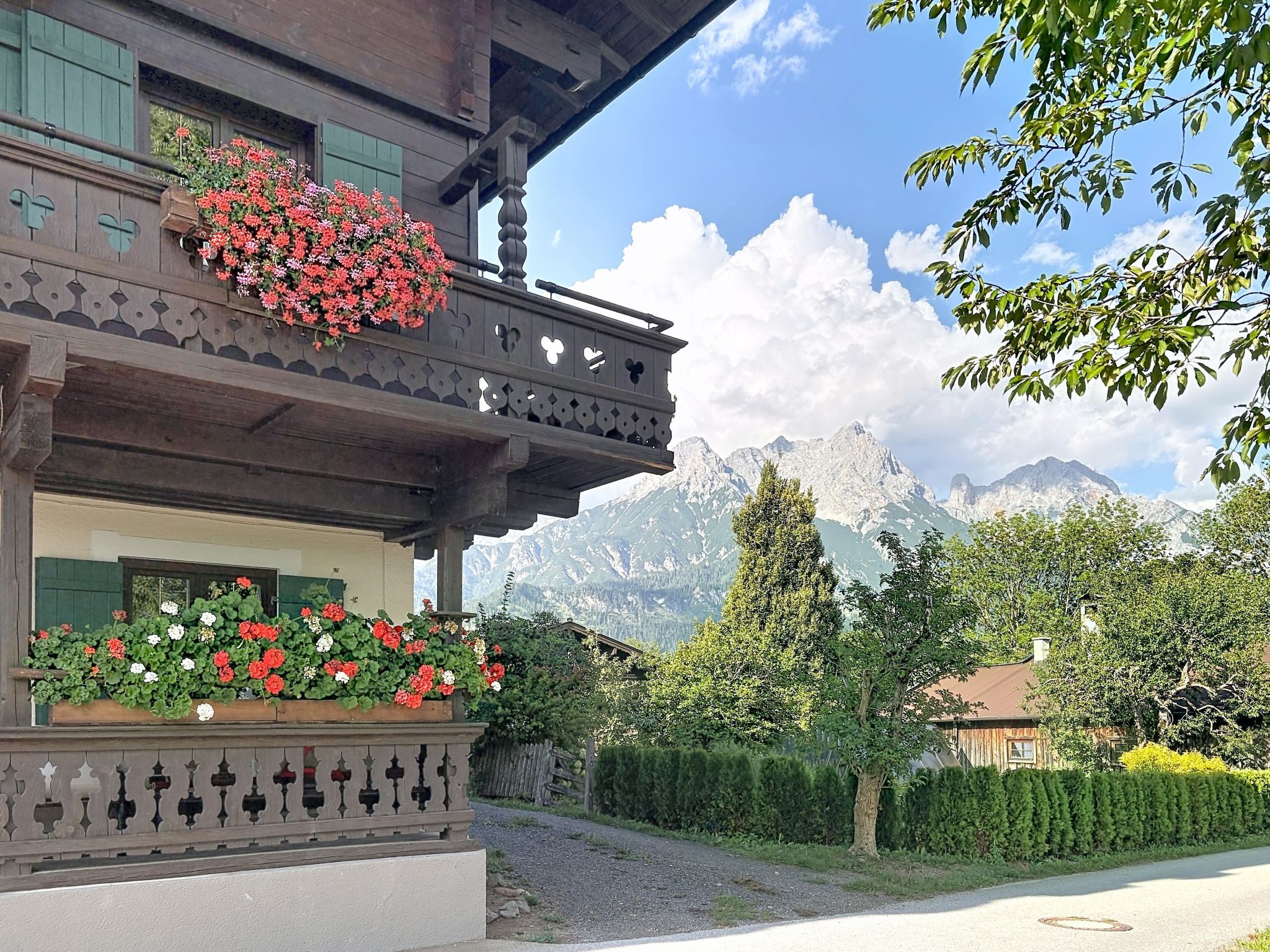 A traditional chalet with a balcony adorned with flowers, set against a backdrop of mountains.