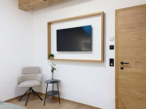 A modern room with a mounted flat-screen TV, a wooden door, a small table with a vase, and a grey armchair. - Thorermartlgut incl. Gästekarte by Interhome (Saalfelden am Steinernen Meer)